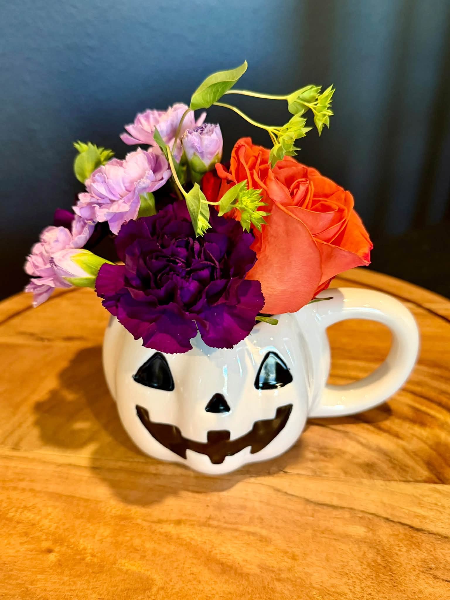 Purple and orange flowers in a white pumpkin mug